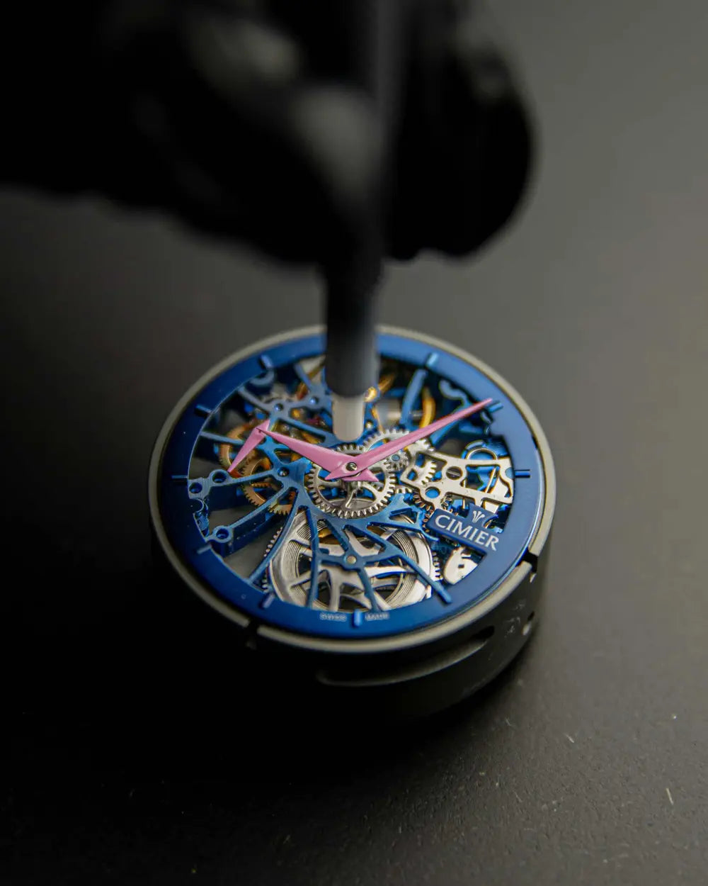 Close-up of a Cimier Royal Skeleton mechanical watch movement being assembled, blue open-worked movement with pink hands