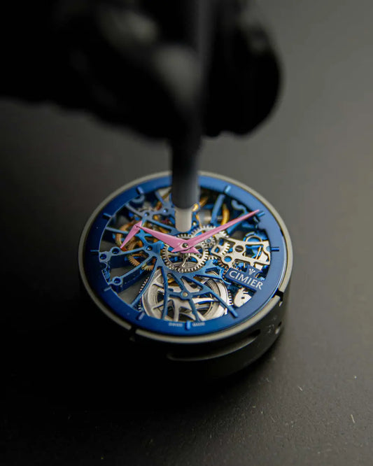 Close-up of a Cimier Royal Skeleton mechanical watch movement being assembled, blue open-worked movement with pink hands