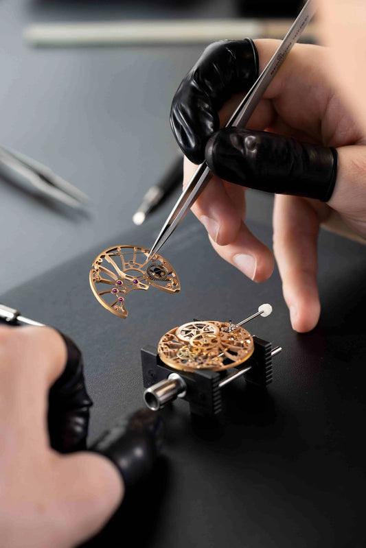 Master watchmaker assembling a skeletonized gold movement at the Watch Academy by Cimier, Swiss watchmaking workshop in Biel